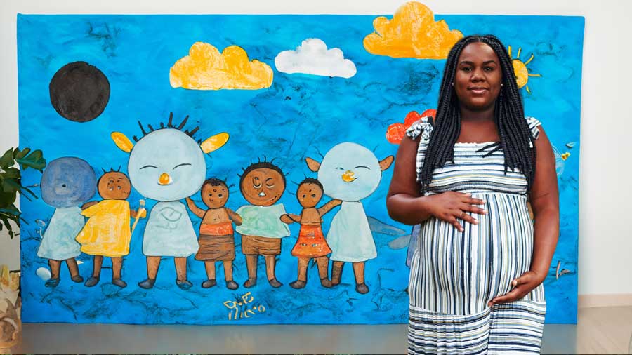 pregnant african american woman in front of a blue child painting depicting several children dancing