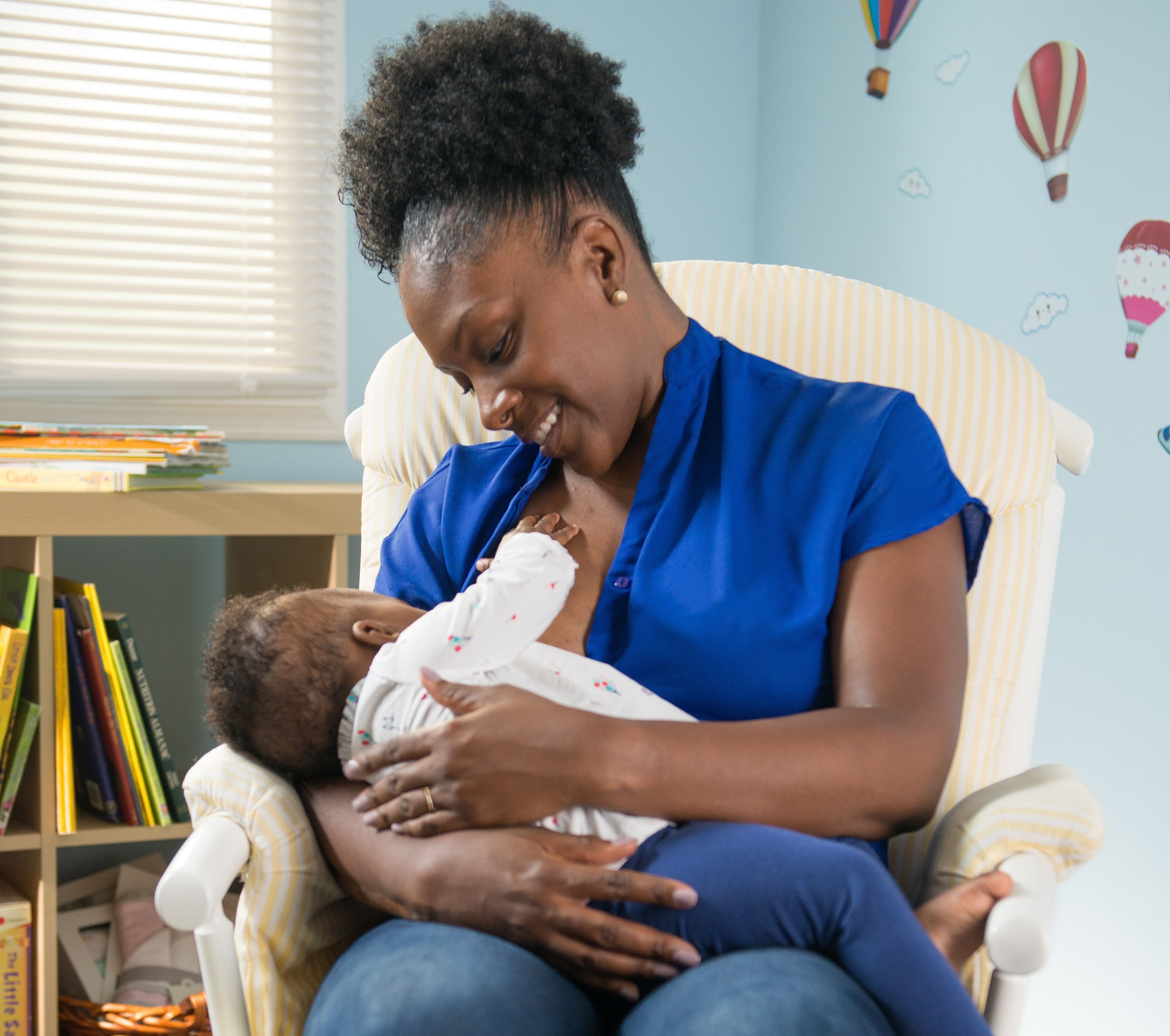 african american woman breastfeeding an infant while seated in a white chair in a room painted in blue